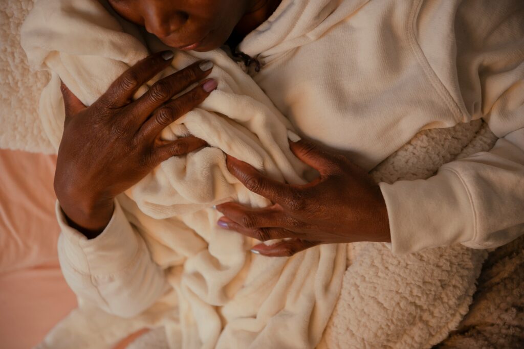 A black person wearing white cozy clothes and holding a newborn to their chest. The photo is taken from slightly above the person.